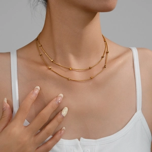 Detail of layered gold snake chain necklace with small cube beads on female model