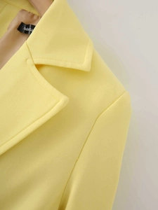 Detailed close-up of yellow satin blazer lapel with high-quality stitching and fabric texture