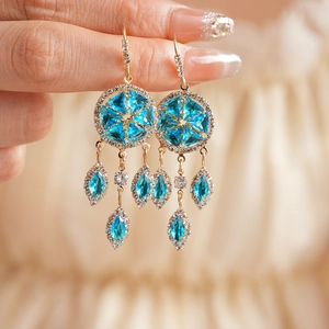 Detail of vintage gold earrings with light blue zircons and rhombus tassel pendants