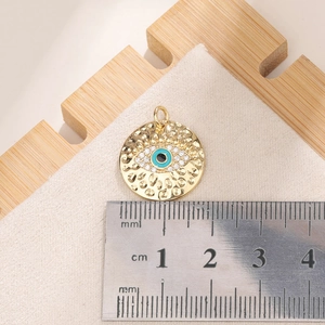 Golden Turkish Evil Eye charm with blue cubic zirconia stones shown with ruler for scale