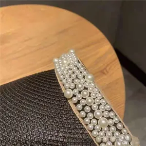 Macro detail of elegant cream pearls hand-sewn onto black straw sun hat brim