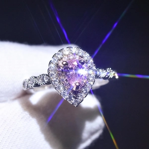 Macro shot of a pear-cut pink moissanite ring with a halo setting on a gloved hand