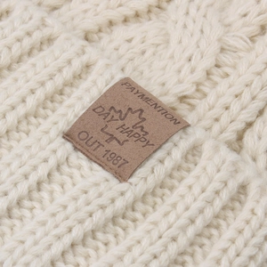 Detailed macro view of the thick knit texture and leather brand patch on the beige winter beanie