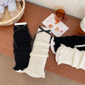 Detail of ribbed knit leg warmers with bow ties and ruffled edges on a wooden table