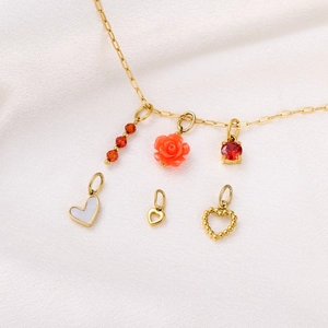 Detail of gold charms including red beads, floral pendant, and shell hearts on silk