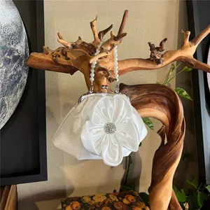 Detailed view of a white satin evening bag featuring a pleated flower and pearl handle