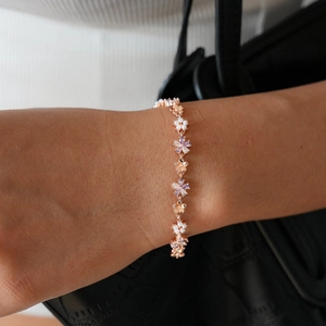 Detail of rose gold flower bracelet with pearls and purple crystals on a leather bag