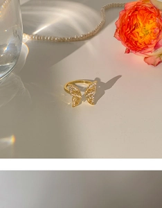 Golden butterfly ring with crystals next to pink roses and pearls in natural light