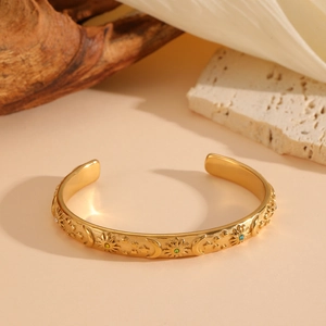 Golden celestial open bangle featuring embossed sun moon and star motifs with colored stones