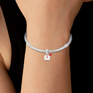 Silver bracelet with medical kit charm featuring a red cross and heart on a model