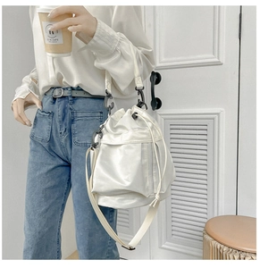 White nylon drawstring bucket bag detail with black metal rings and adjustable strap