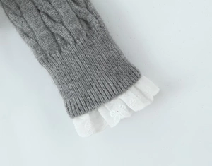 Detail of cable knit texture with white floral lace trim on a grey sweater sleeve