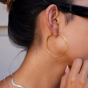 Close-up of a model wearing large polished gold stainless steel hoop earrings for women