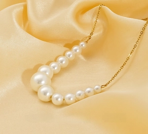 Detail of gradient pearl necklace with gold stainless steel chain on yellow silk cloth
