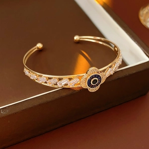 Dettaglio del bracciale aperto dorato con occhio blu e zirconi rettangolari lucidi