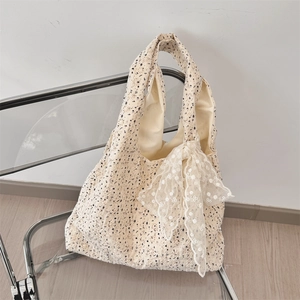 Detail of floral canvas tote bag with a white lace bow hanging on a modern chair