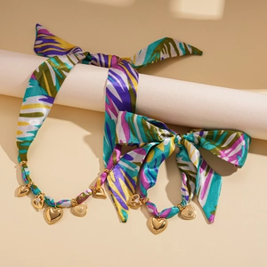 Macro detail of silk scarf necklace featuring golden heart charms and vibrant print