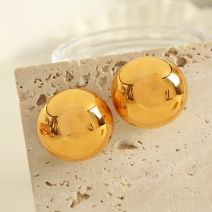 Minimalist gold eggshell ball stud earrings on a textured stone display pedestal