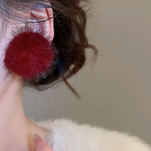 Gros plan de boucles d'oreilles boules en fausse fourrure bordeaux portées par un mannequin