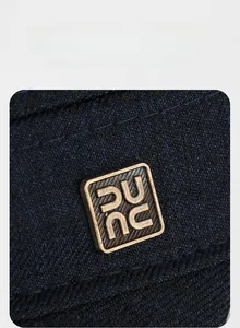 Close-up of golden rectangular metal logo on navy blue twill fabric of the flat top cap