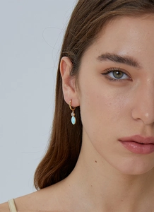 Close-up of gold-plated hoop earrings with light blue drop and sparkling zircon on model