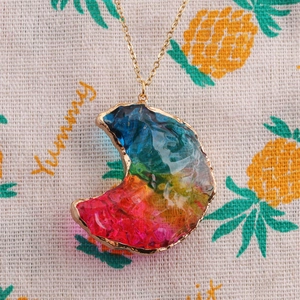 Détail d'un pendentif en forme de croissant avec résine irisée et chaîne dorée