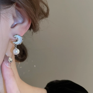 Close-up of crescent moon earrings with cubic zirconia and white pearls on a model