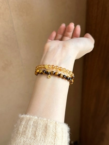 Close-up of layered tiger eye and citrine beaded bracelets with golden charms on wrist