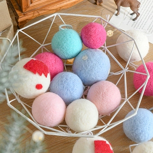 Handmade wool felt Christmas balls in assorted colors inside a metal basket on wood background