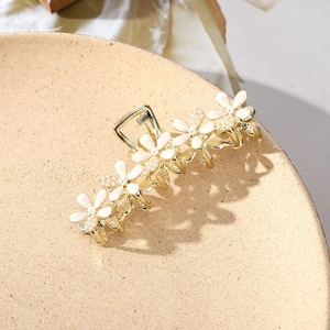 Detailed macro view of golden metal hair claw with white flowers and faux pearls decoration