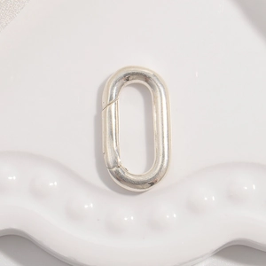 Macro shot of silver oval spring clasp connector on a white ceramic tray for jewelry making