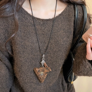 Detail of plush triangle pendant necklace with silver chain on brown sweater