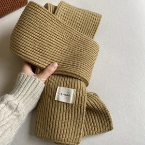 Close-up of camel-colored ribbed knit texture and h.modmi brand tag on winter scarf