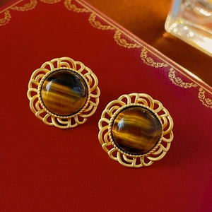 Macro shot of vintage gold earrings with tiger eye stone on a textured red gift box
