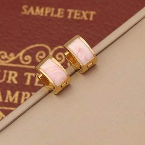 Macro shot of gold-plated huggie earrings with pink marble resin texture on tan background