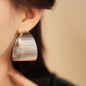 Detail of silver C-shaped earrings with textured horizontal stripes on female model