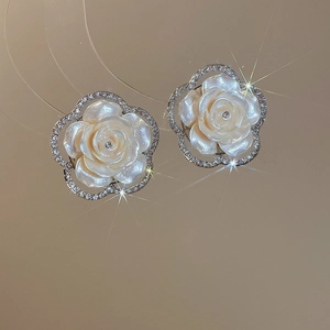 Detailed view of white resin camellia earrings with shell luster and diamond-studded edges