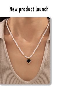 Detail of pearl necklace with a black heart pendant and gold metal accents on model
