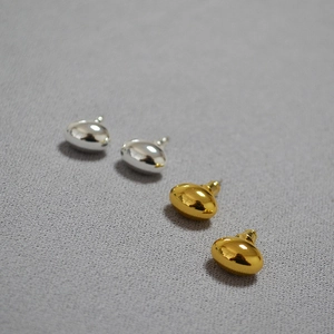 Macro detail of organic gold and silver bean stud earrings on grey fabric background