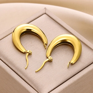Close-up of polished gold U-shaped hollow earrings on a textured jewelry box