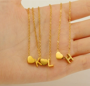 Close-up of golden stainless steel heart necklaces with letter pendants held in palm