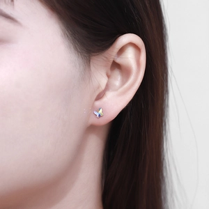Close-up of a holographic butterfly stud earring worn on ear with iridescent finish