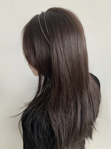 Detail view of a slim silver metal headband styled on long dark hair against a white wall