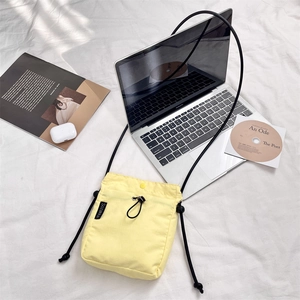 Piccola borsa a tracolla giallo chiaro minimalista con cordino regolabile su sfondo di tessuto