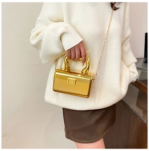 Close-up of golden metallic mini hard-shell clutch bag with handle and fine chain strap