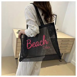 Woman carrying large black mesh tote bag with pink Beach Vibes print in a bright room
