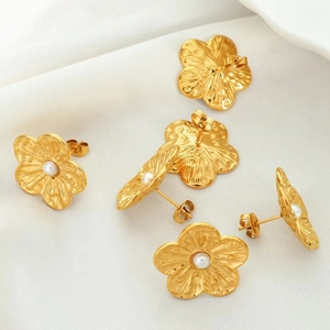 Detailed view of gold flower earrings with pearls on white silk background