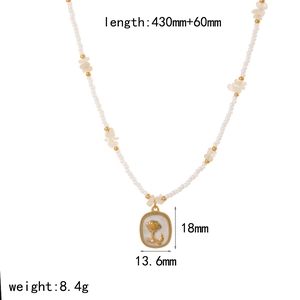 Dettaglio della collana con ciondolo a rosa dorata e perle bianche su uno sfondo semplice