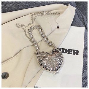 Detail of silver heart shell metal evening bag with bead chain on beige blazer jacket
