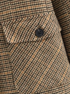 Nahaufnahme von Tweed-Blazer-Stoff mit Hahnentrittmuster, schwarzem Knopf und Tasche